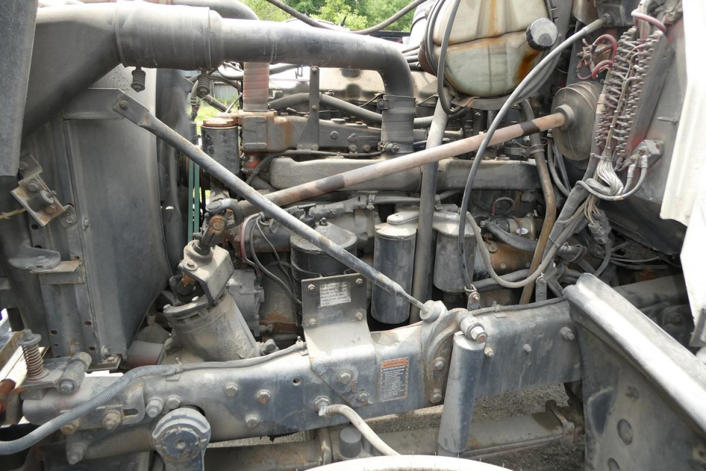 Mack RD690S engine bay showing diesel engine components, hoses, and radiator area in a used flatbed truck.