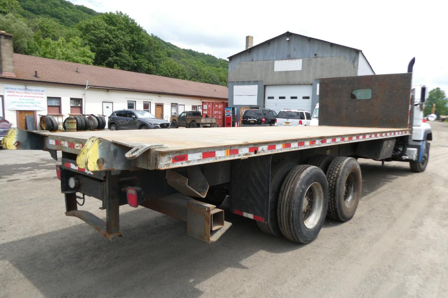Flatbed truck rear view showing triple axle wheels and loading bed with raised rear bumper and taillights.