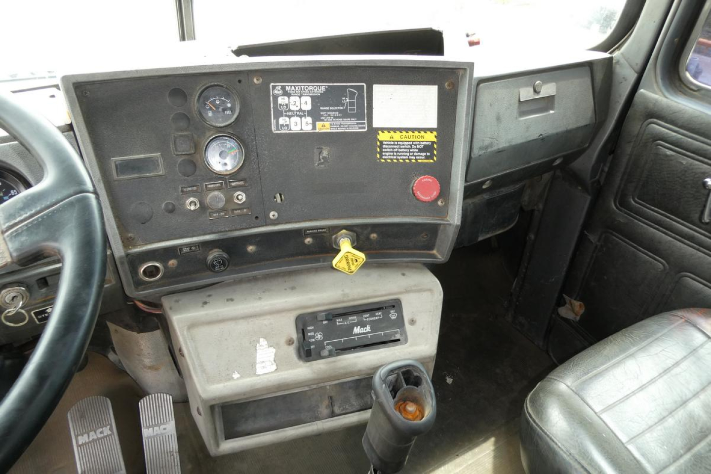 Interior dashboard of a Mack RD690S showing gauges, steering column, ignition key, and center console with switches and a cup holder.