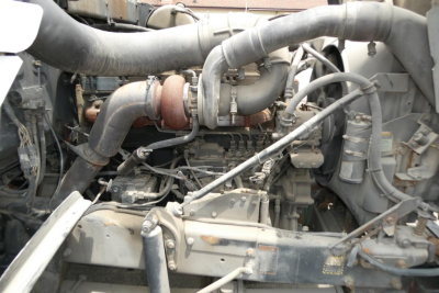 Mack RD690S engine bay with turbocharger, hoses, and intake pipes visible in a dusty in-service condition.