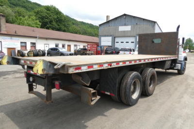 Flatbed truck rear view showing triple axle wheels and loading bed with raised rear bumper and taillights.