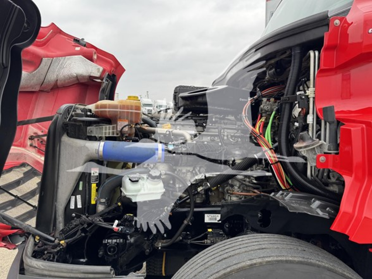 Truck engine bay of 2023 Freightliner Cascadia 126 with exposed components and wiring; visible coolant reservoir, hoses, and engine blocks.