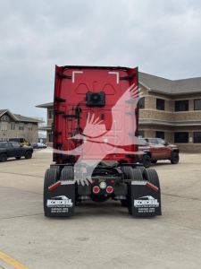 Freightliner Cascadia rear view showing red cab, dual rear tires, black fenders, and mudflaps with Kordell sign in a dealership lot.