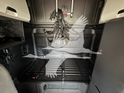 cab interior of a Freightliner Cascadia 126 sleeper showing overhead panels, dashless view, and cargo area with a protective mat and straps