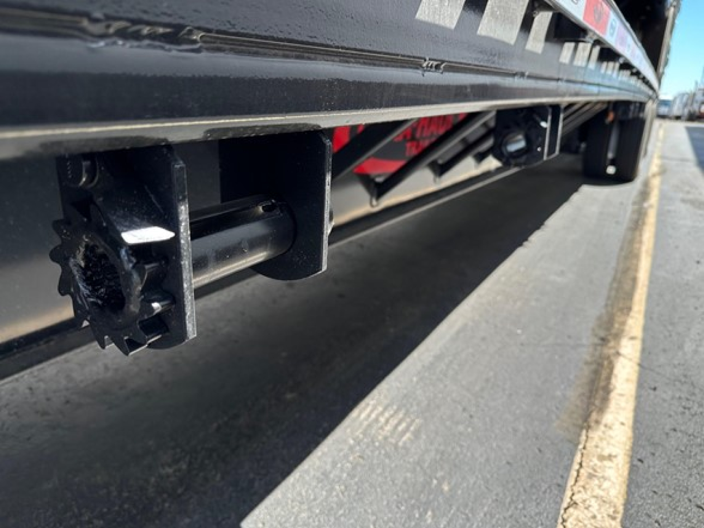 Trailer undercarriage showing mounting hitch area and black steel drop deck frame with a beavertail mechanism visible.