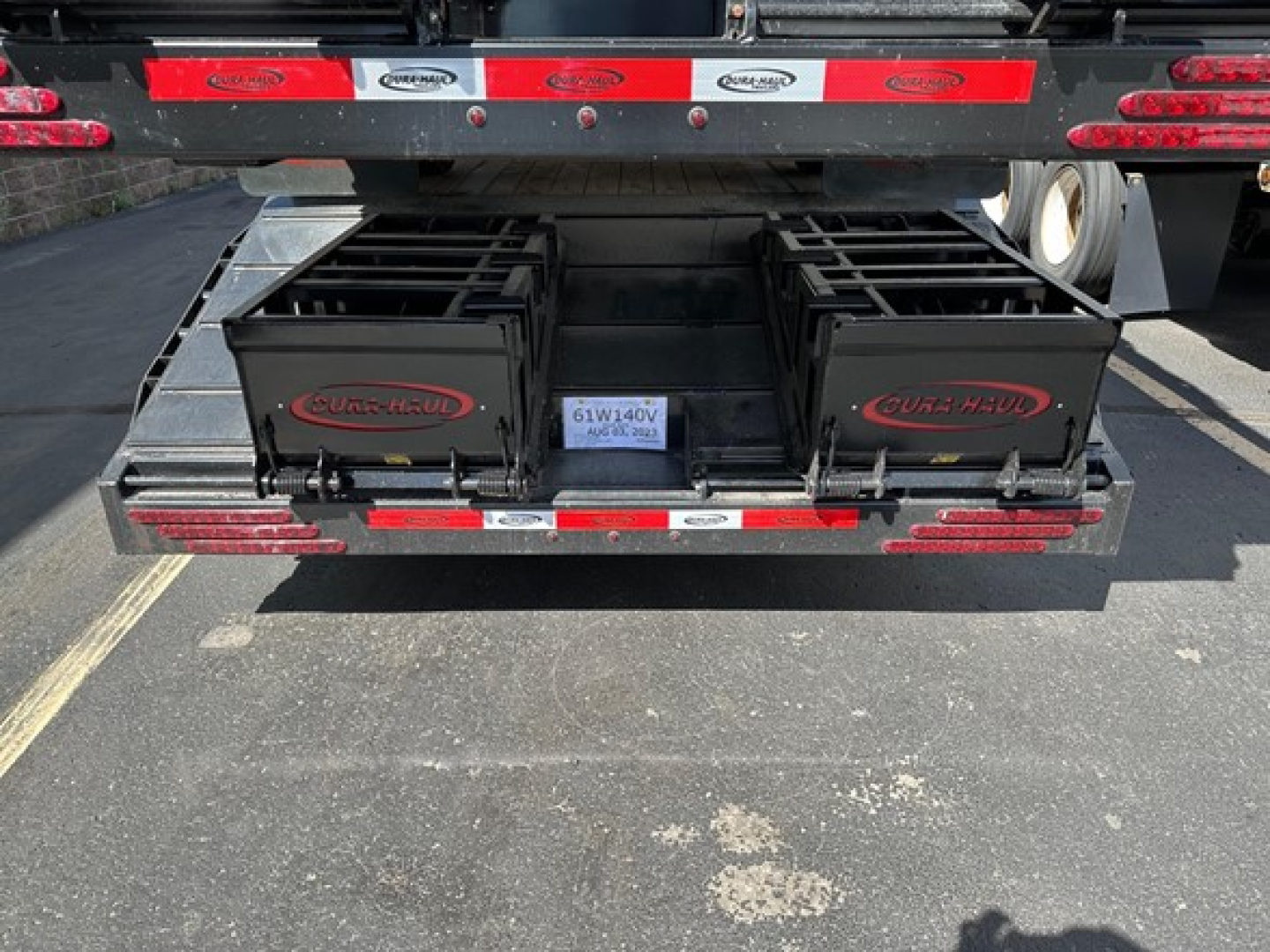 Rear view of a new 2027 Dura Haul steel drop deck trailer with beavertail, showing two black tool boxes labeled DURAHAUL and a center plate with VIN/stock. Tail lights and reflective tape visible.