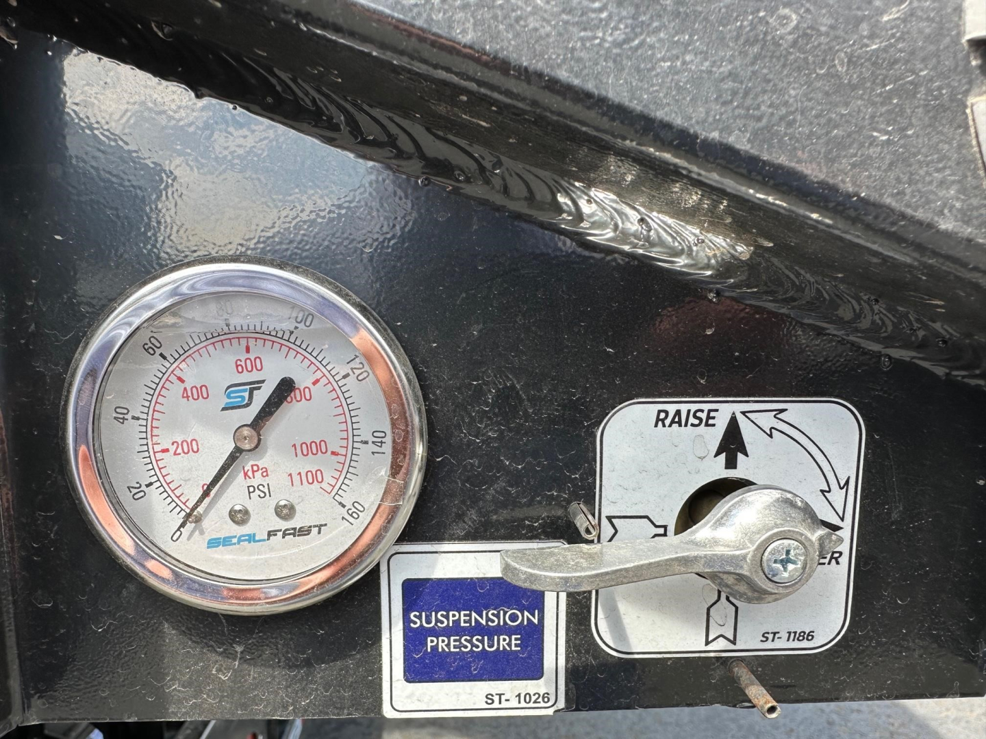 Panel with a round pressure gauge showing PSI numbers and a metal lever labeled suspension pressure with a blue ST label nearby.