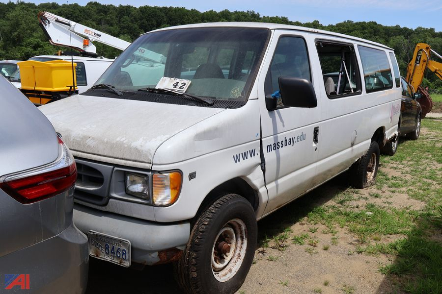 Ford E-Series cargo van side view showing MassBay van with open passenger door and a dented front, white color, in a lot.