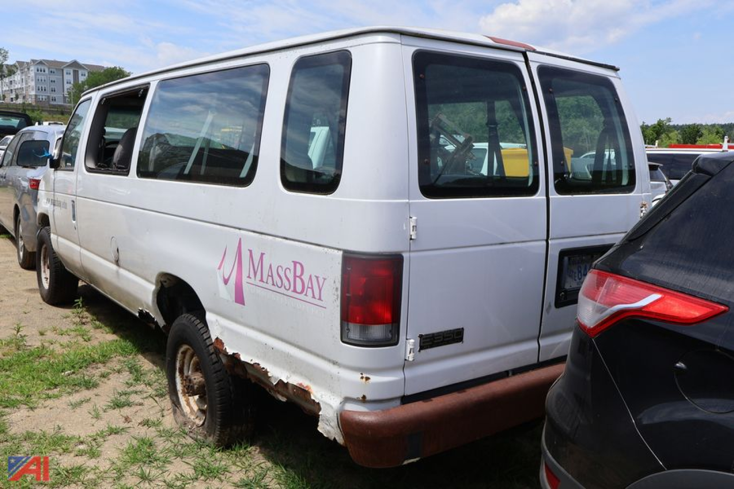 Ford E350 cargo van with MassBay logo showing side and rear windows, rear bumper rust marks, in a lot with other vehicles.