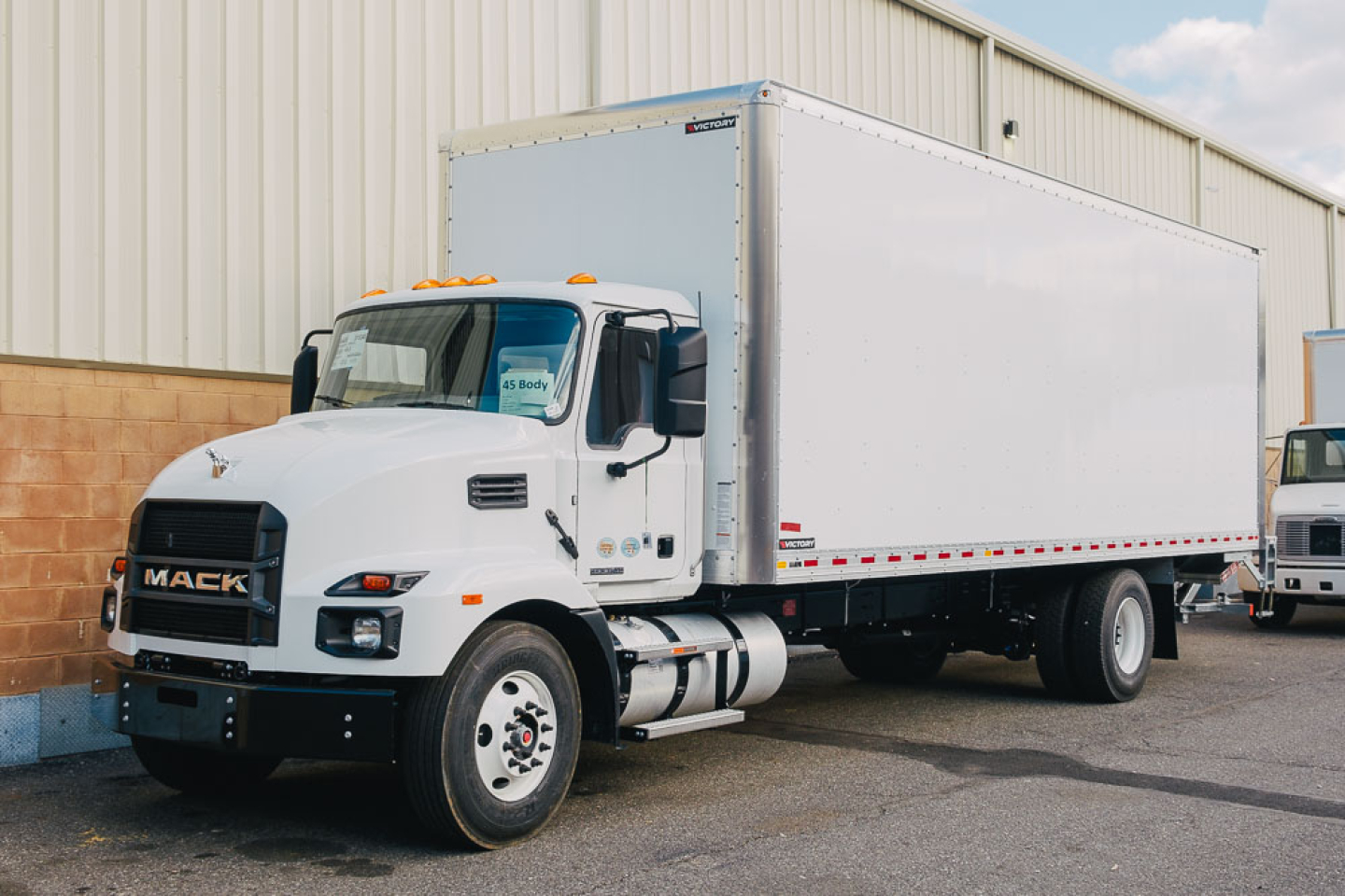 White 2025 Mack MD6 box truck viewed from front-left showing cab and large rectangular cargo box