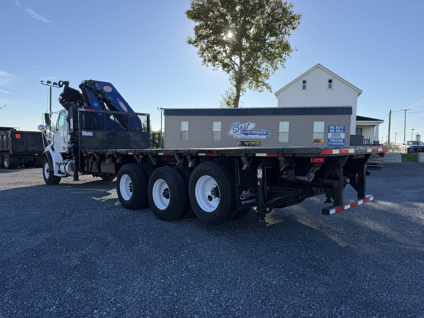 Truck-mounted boom flatbed trailer showing Sterling LT9500 with crane and side signs.
