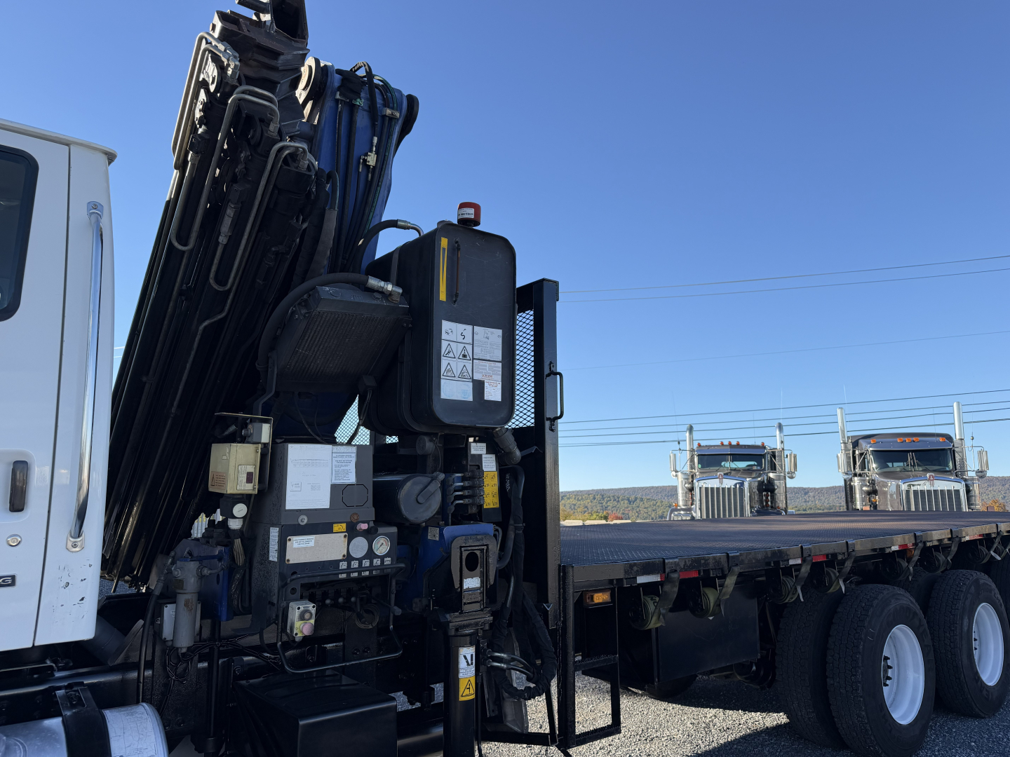 Sterling LT9500 boom truck with hydraulic crane mounted on a flatbed trailer, side view showing control panel, warning stickers, and multiple tires in background.