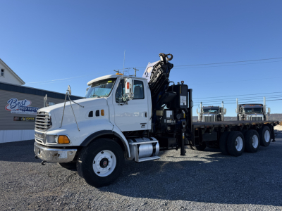 2006 Sterling LT9500 truck with a boom and crane, white cab, flatbed with multiple axles, on a gravel lot.
