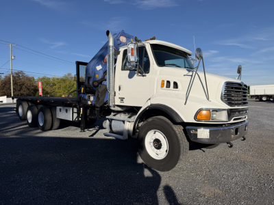 Truck-mounted crane boom truck showing Sterling LT9500 cab with crane behind cab, side view of front wheel and bumper, clear sky.