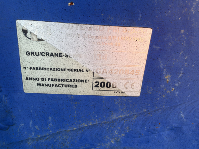 Vehicle label on blue machinery showing model/manufacturer plate with serial numbers and year 2006, worn corner, white label with black text.