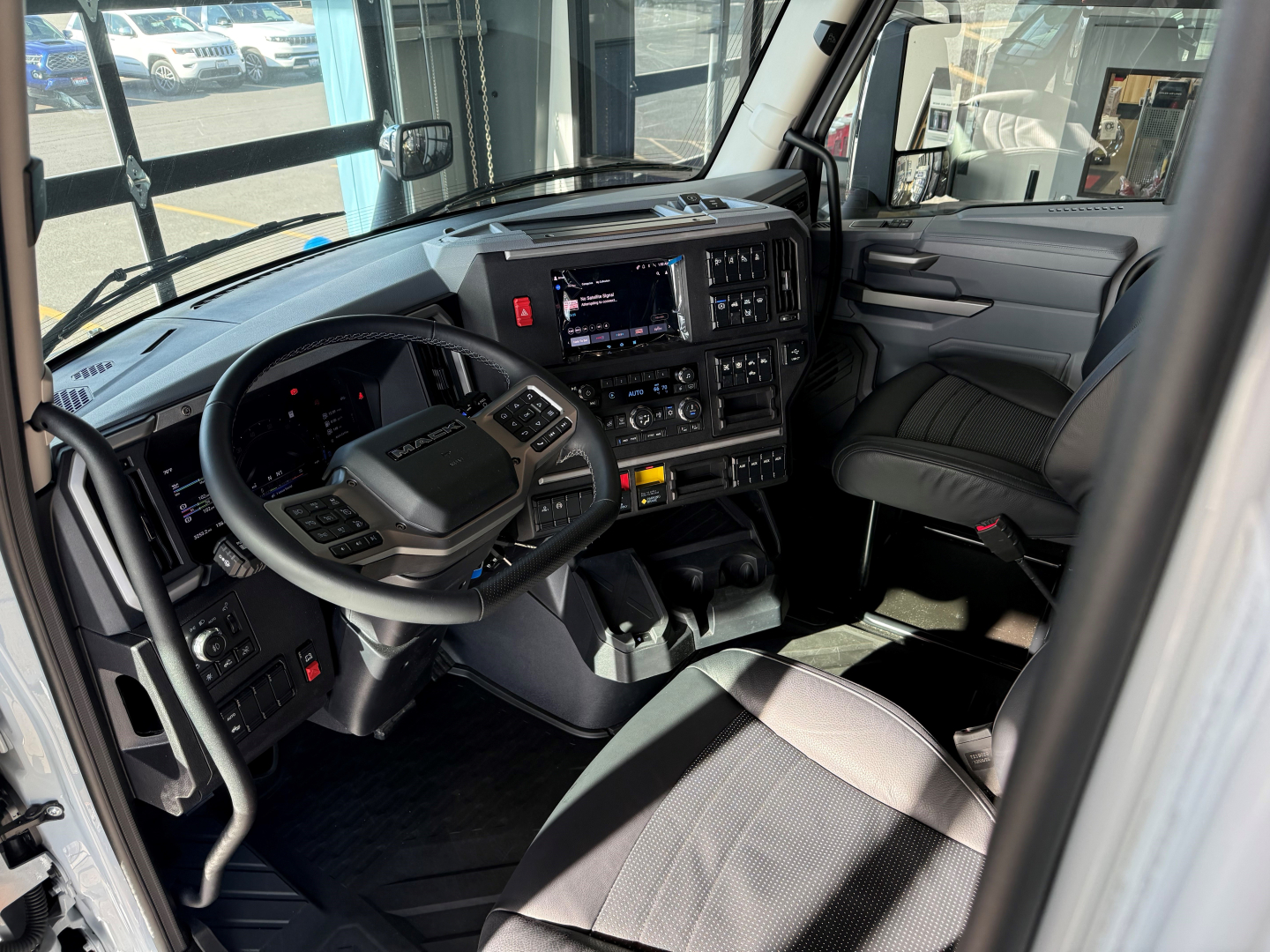 Truck cabin interior showing steering wheel and dashboard with digital displays and controls in a new Mack AN64T64 sleeper cab.