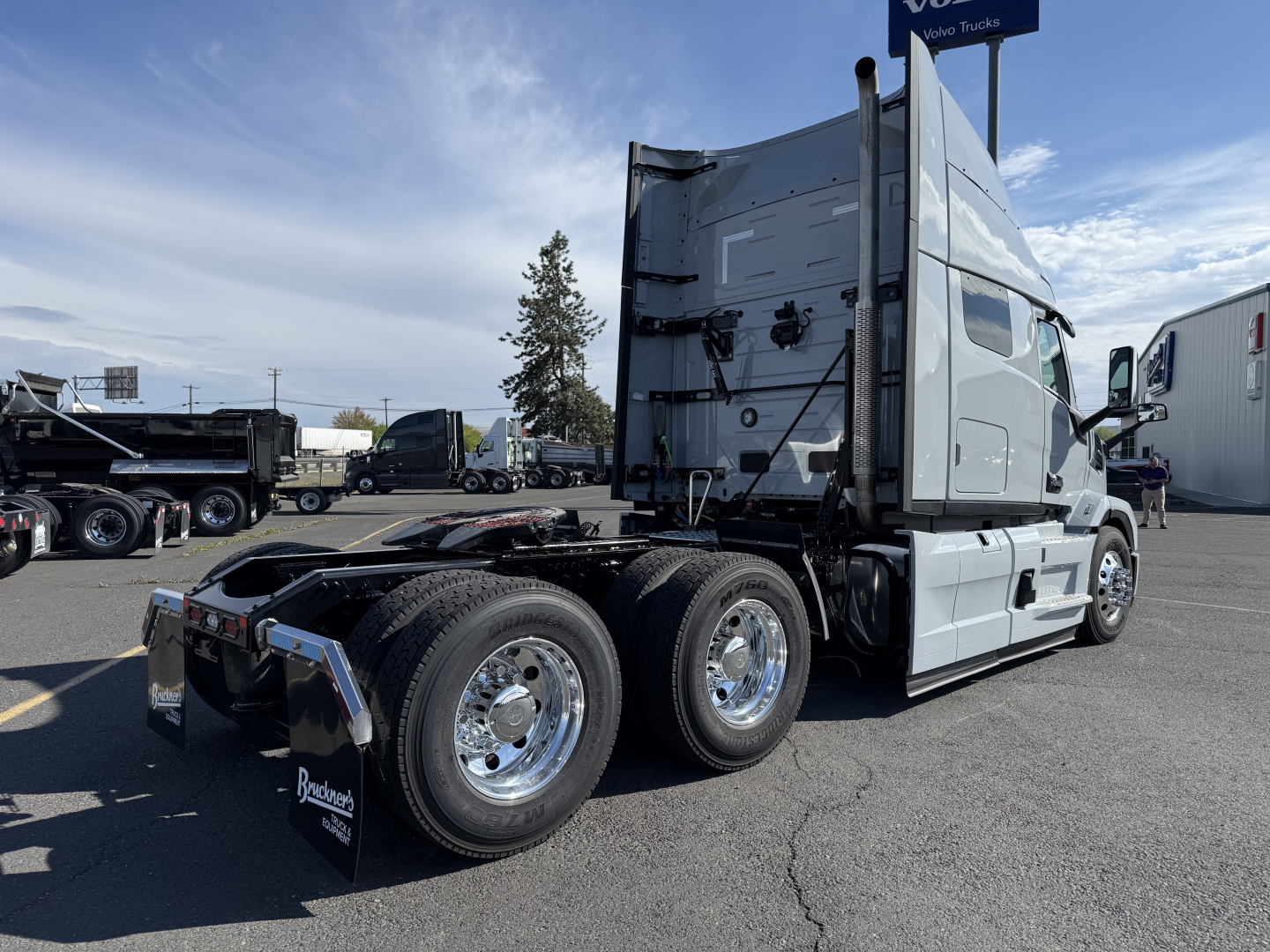 Truck: Mack AN64T64 conventional sleeper tractor, side view with three-axle rear and dual rear tires, silver cab, chrome wheels, blank trailing equipment, parking lot.