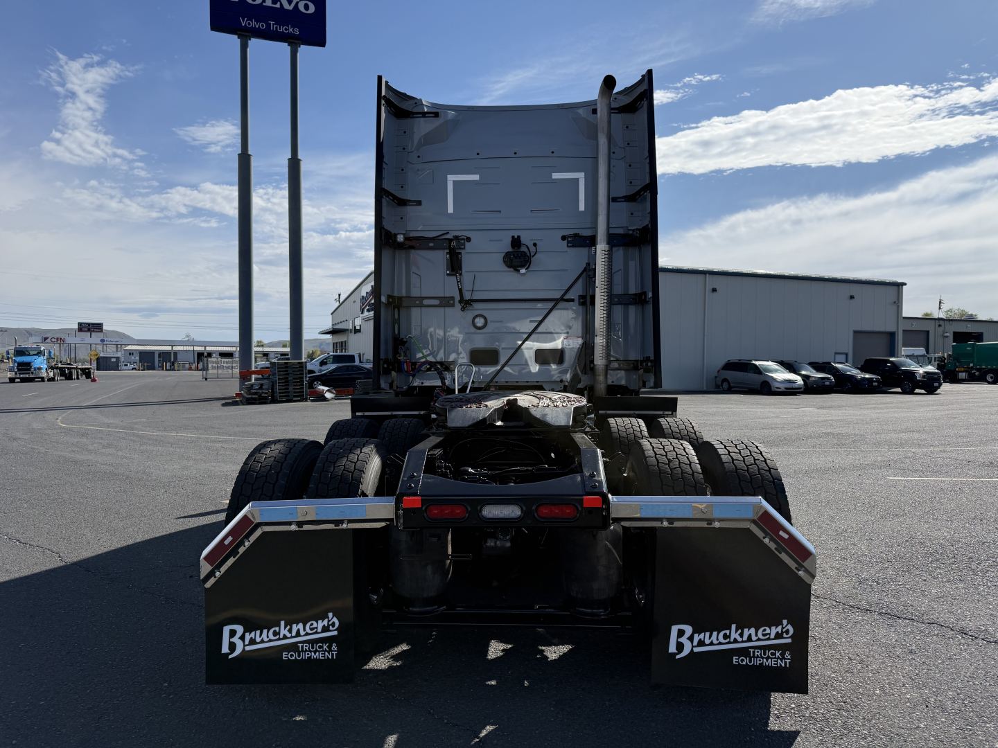 Truck tractor rear view showing fifth wheel and dual rear axles, mudflaps with Bruckner Truck Equipment logo, clear sky, dealer lot in background.