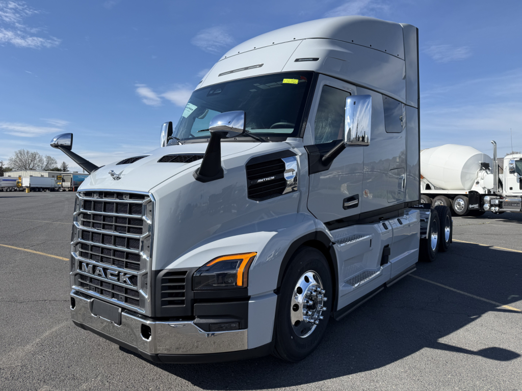 Mack AN64T64 conventional sleeper truck in a parking lot, chrome grille with Mack emblem, large side mirrors, dual rear axles, aerodynamic sleeper cab, front view.
