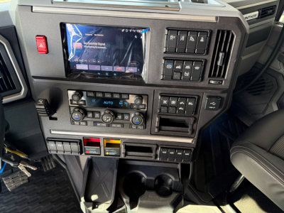 Dashboard of a new 2027 Mack AN64T64 showing touchscreen infotainment, climate controls, and multiple control switches; VIN 1M1A24GY7VM102395 and stock number 72579 in view.