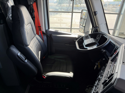Cab interior of a new Mack AN64T64 conventional sleeper truck showing driver seat, steering wheel, and dashboard with multiple control panels.