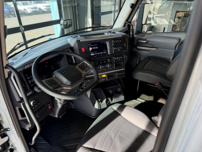 Truck cabin interior showing steering wheel and dashboard with digital displays and controls in a new Mack AN64T64 sleeper cab.