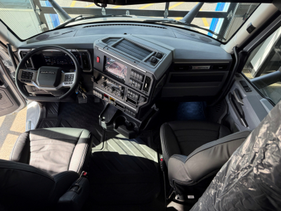 Cockpit view of a Mack truck interior showing dashboard with touchscreen display, steering wheel, and driver and passenger seats.