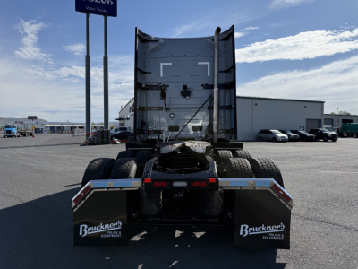 Truck tractor rear view showing fifth wheel and dual rear axles, mudflaps with Bruckner Truck Equipment logo, clear sky, dealer lot in background.