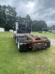 Kenworth T800 tractor chassis with fifth wheel and dual rear axles in a grassy lot, rear view showing hitch and hydraulic lines.