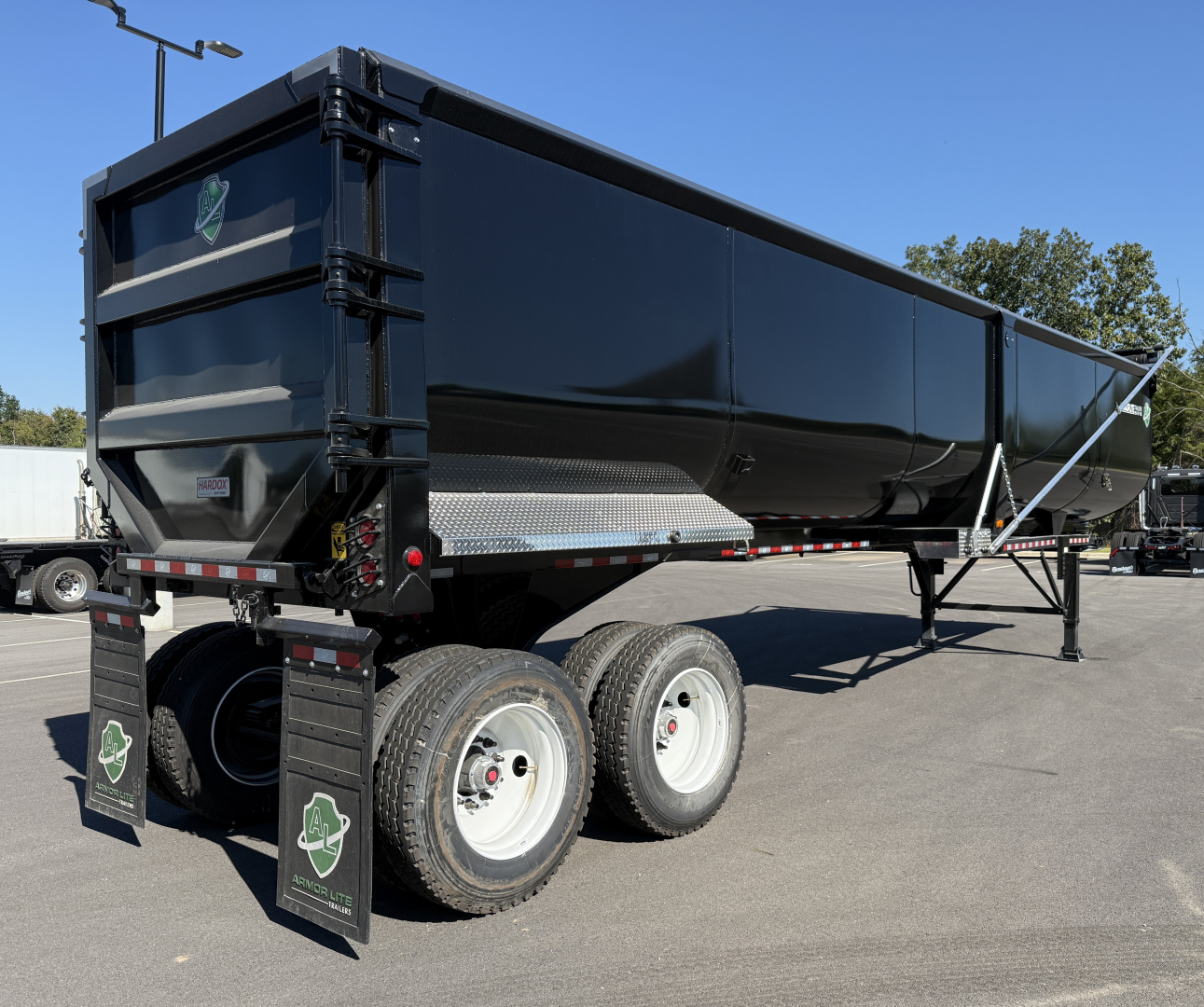 Armored Armor Lite dump trailer showing black rectangular dump body with dual rear wheels and side chrome step, tires, and green emblem mud flaps.