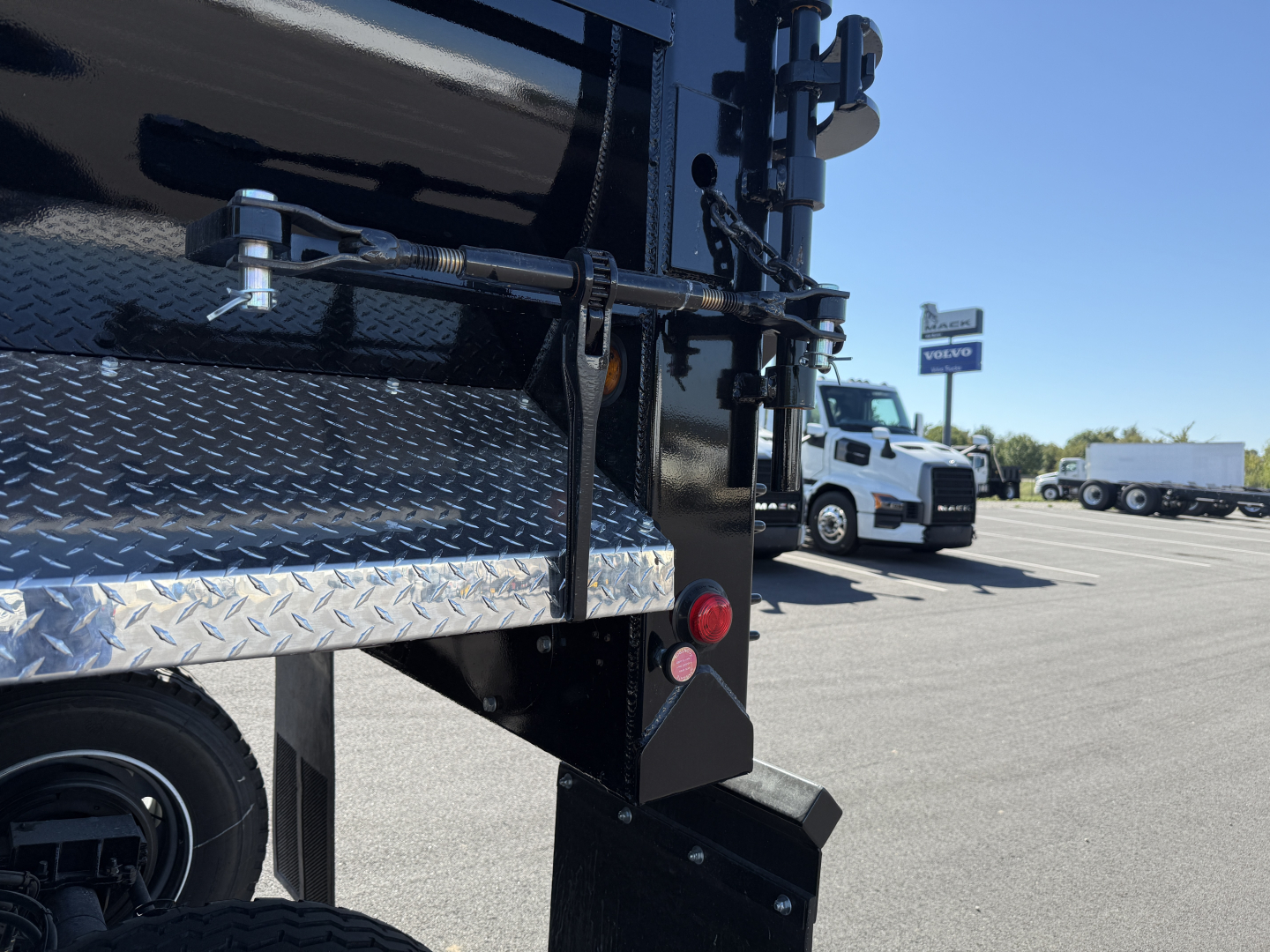 Armor Lite dump trailer rear corner showing diamond plate fender and taillight, black paint, and rear bumper.
