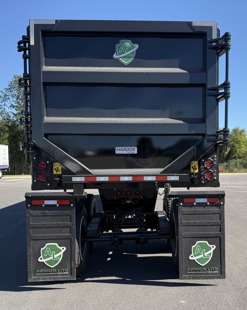 Dump trailer rear view showing Armor Lite branding and mudflaps with green shield logo; dual axles, rear underride guards, and Hardox label on the tailgate.