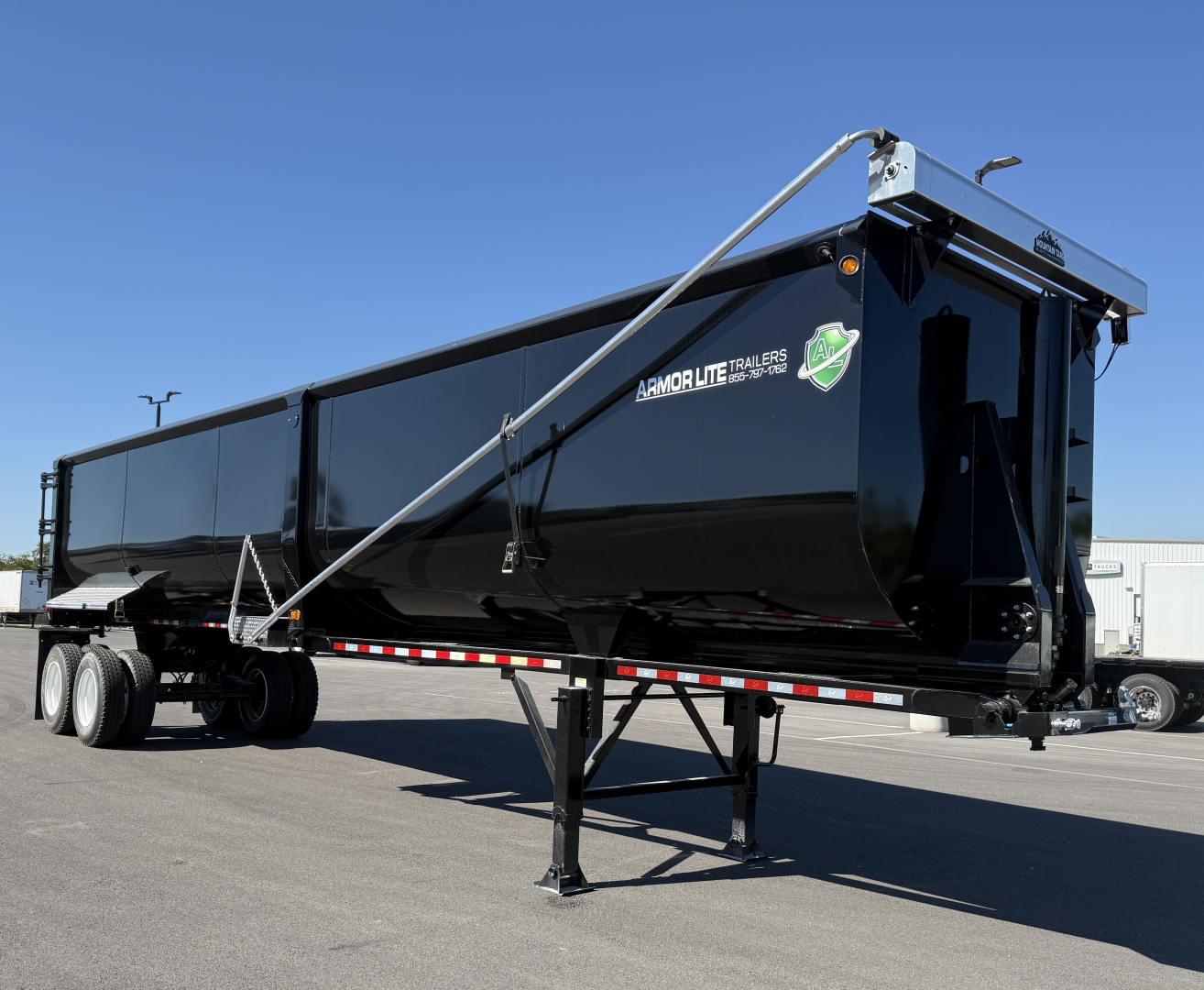 Armor Lite trailer showing black dump trailer with raised front hitch and landing gear, 40' long, with logo and striped reflective tape.