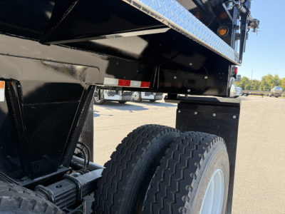 Dump trailer undercarriage showing dual rear tires and suspension, black frame, and reflective tape on side rail.