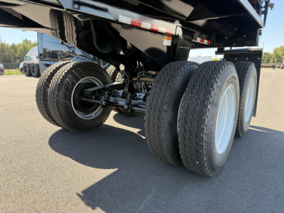 Trailer rear view showing dual rear tandems and dump trailer chassis with black painted frame and white spoke wheels.