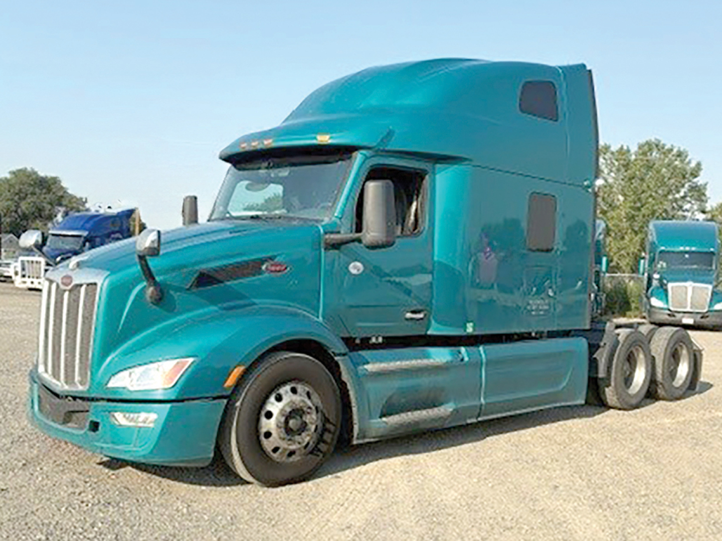Peterbilt 579 truck in teal color, semi-truck tractor in a lot, front left view.