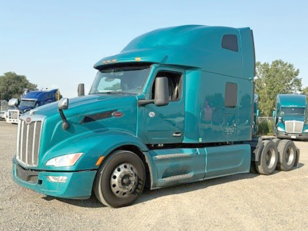 Peterbilt 579 truck in teal color, semi-truck tractor in a lot, front left view.