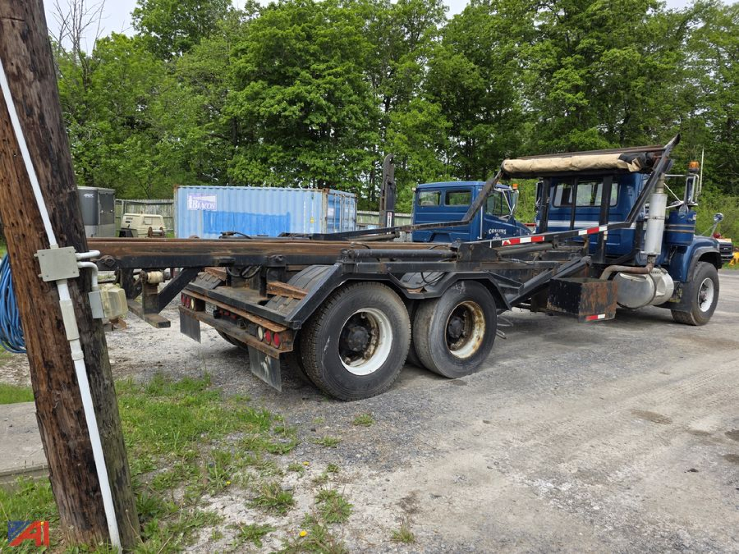 1987 Mack RD688S roll off truck showing blue cab and long trailer frame with rear dual wheels and hoist assembly.
