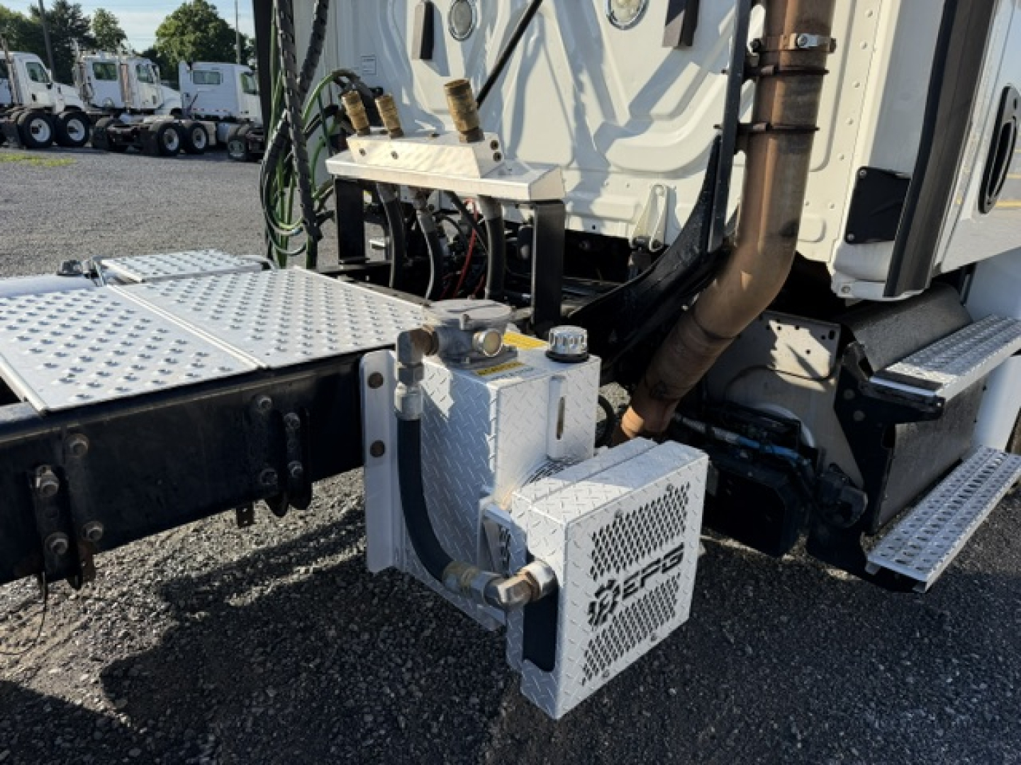 Truck engine bay area of a Freightliner Cascadia 125DC showing auxiliary fuel or air system with metal braided hoses and mounting plate.