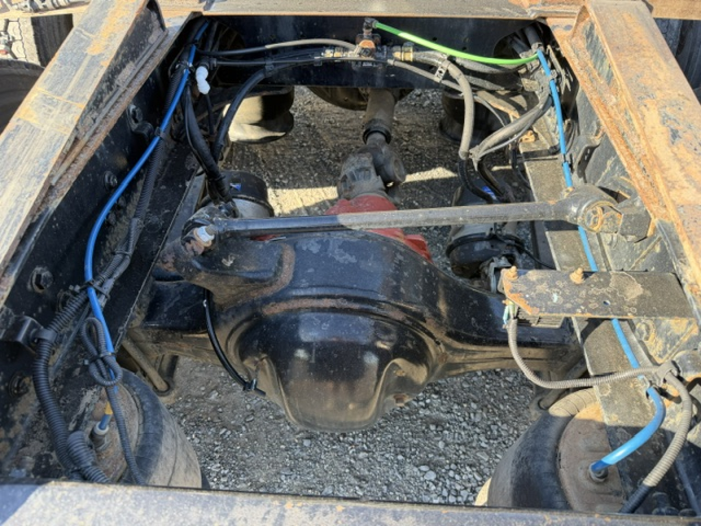 Rear view of a Freightliner Cascadia truck chassis showing the drivetrain with differential and suspension components, blue hoses, and wiring harnesses.