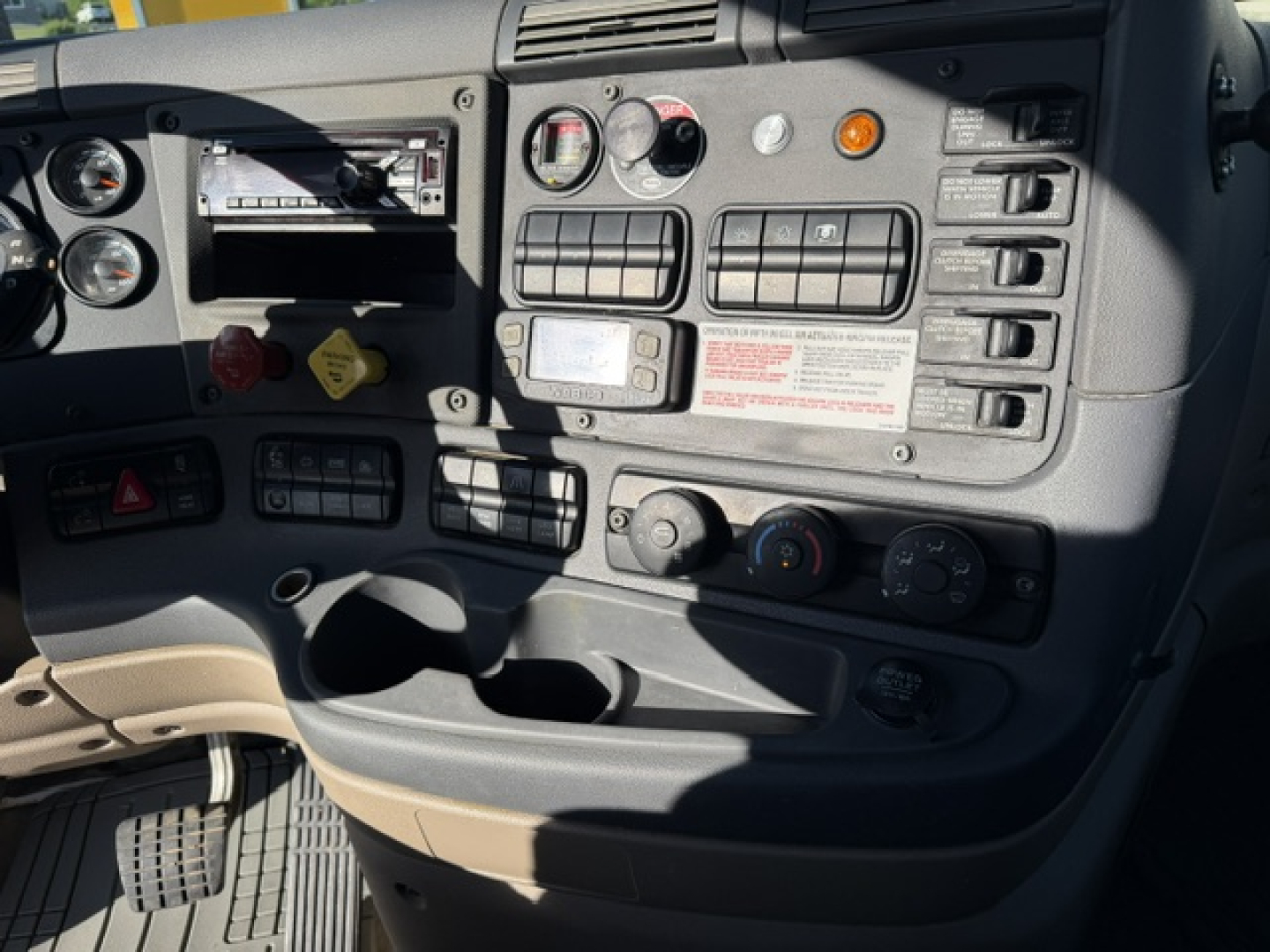 Dashboard of a Freightliner Cascadia 125DC truck showing gauges, switches, and control panel with warning labels and vents.