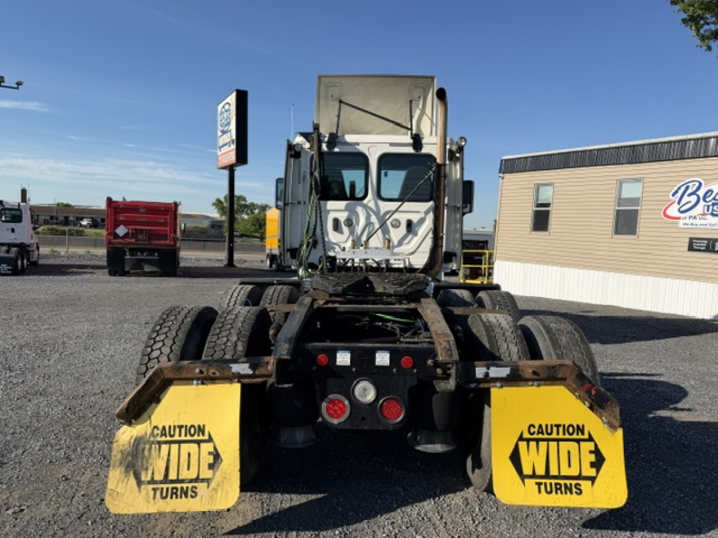 Freightliner Cascadia truck rear view showing bumper, dual rear axles with mud flaps labeled CAUTION WIDE TURNS, various lights and fifth-wheel area.