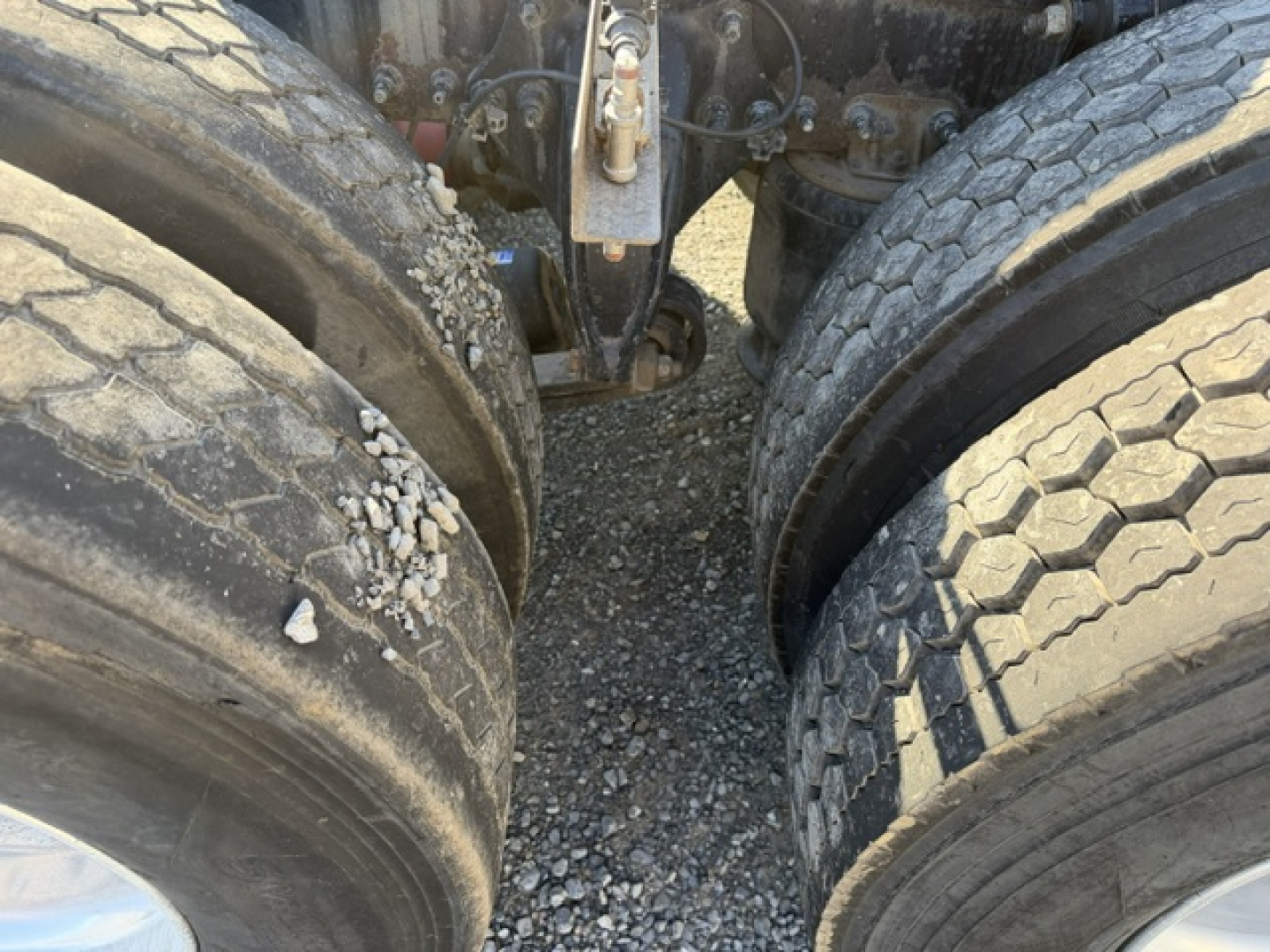 Truck axle area showing Dual rear axles with worn tires, heavy tread, mud and rock debris, fifth wheel area not visible.