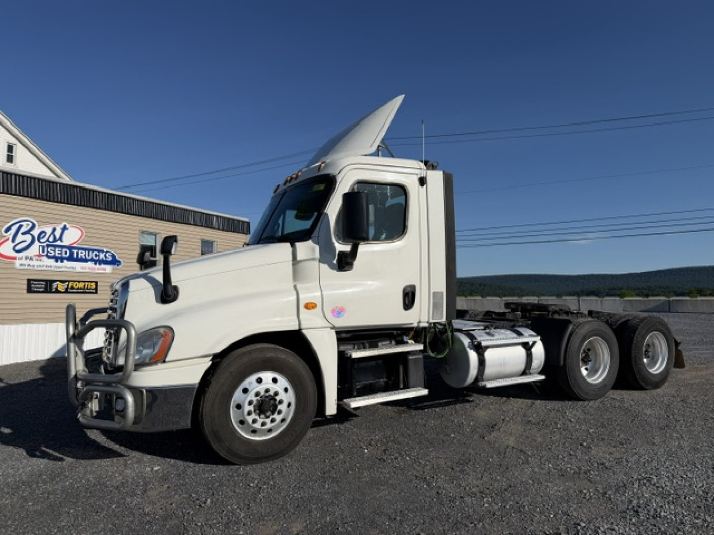 Freightliner Cascadia daycab truck side view showing white cab and chassis with aerodynamic hood and fuel tanks.
