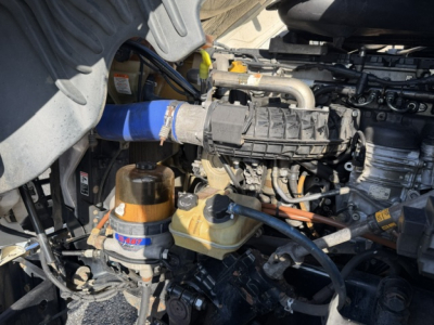 Engine bay of a 2020 Freightliner Cascadia 125DC showing coolant reservoir, power steering fluid reservoir, blue silicone hose, and various engine components.