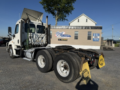 Freightliner Cascadia 125DC chassis in rear view showing dual rear axles and yellow warning placards, with a service building in the background.
