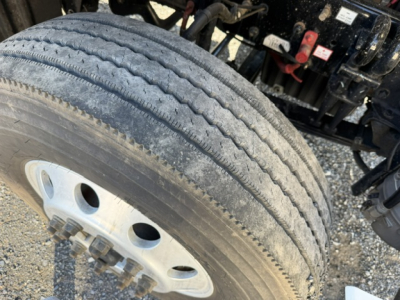 Truck wheel and dual tire setup with a partial view of Freightliner Cascadia front suspension and frame.