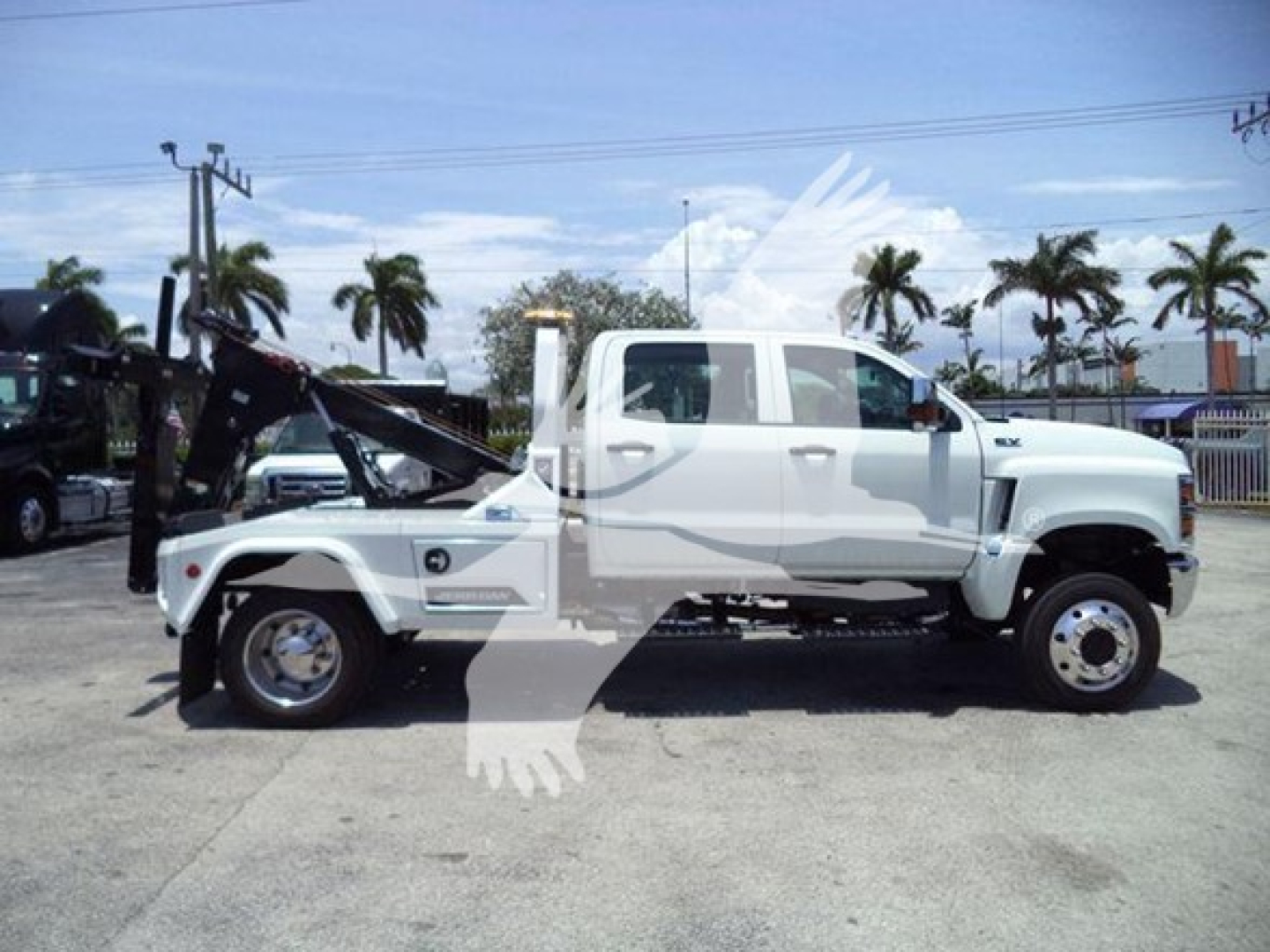 Side view of a white 2023 International CV winch truck with a raised crane/winch apparatus and logo overlays. Visible labels include VIN-like text and stock number overlay.
