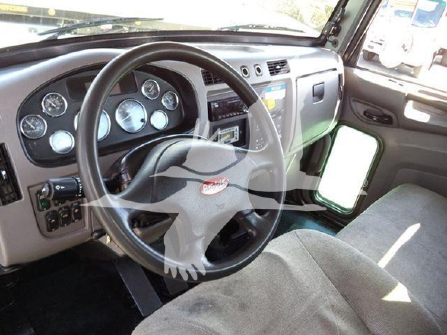 Peterbilt dashboard and steering wheel interior with gauges, pedals, and a side mirror visible.
