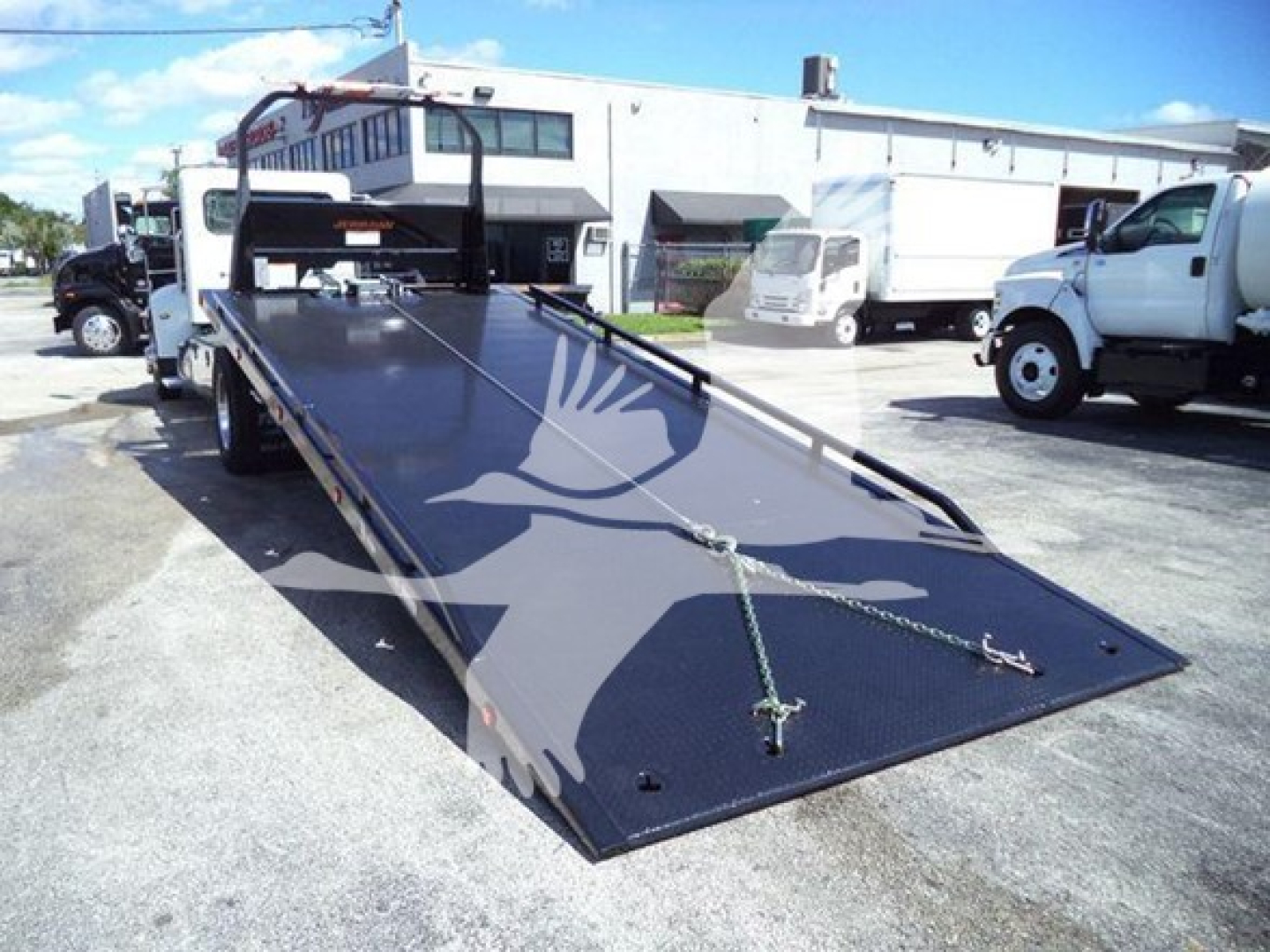 Peterbilt 337 rollback tow truck image showing lengthy black flatbed with ramps and chains, cab in background, used vehicle.